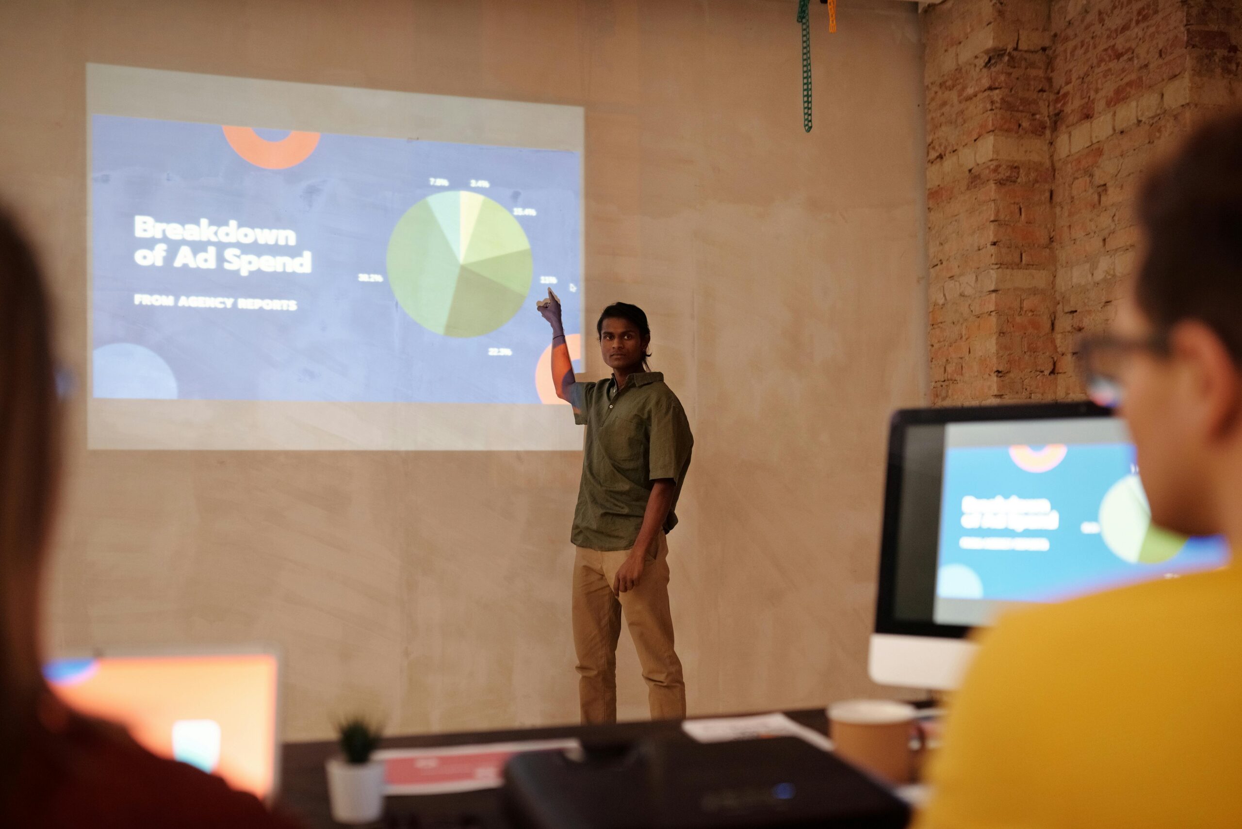 pexels-photo-6476787-6476787 Young man delivering a business presentation on ad spend with charts and graphs in a modern office setting.